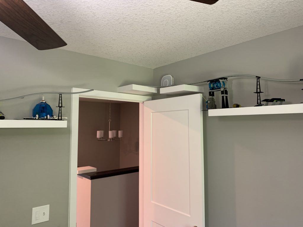 Photograph of shelving installed along fourth and final wall of game room, with track laid out. Almost connected back to the first wall shelving, but not yet.