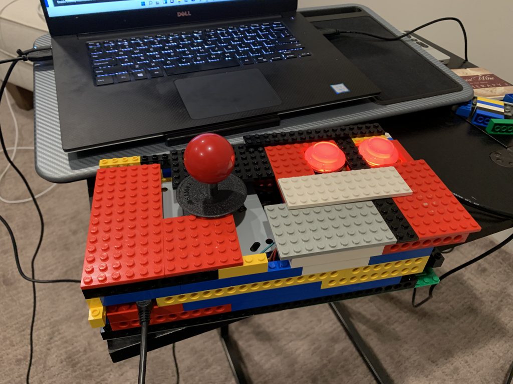 Photo of LEGO and controls wrapped in a pish-posh of LEGO brick, functional, and RGB buttons lit up in red.