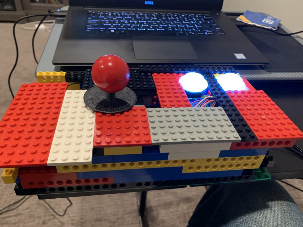Photo of LEGO and controls wrapped in a pish-posh of LEGO brick, functional, and RGB buttons lit up in white.