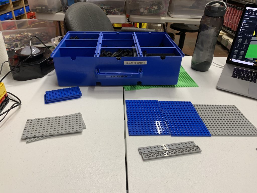 Photo of a table with a few LEGO plates sitting on it and in the background, large buckets of brick, everywhere.