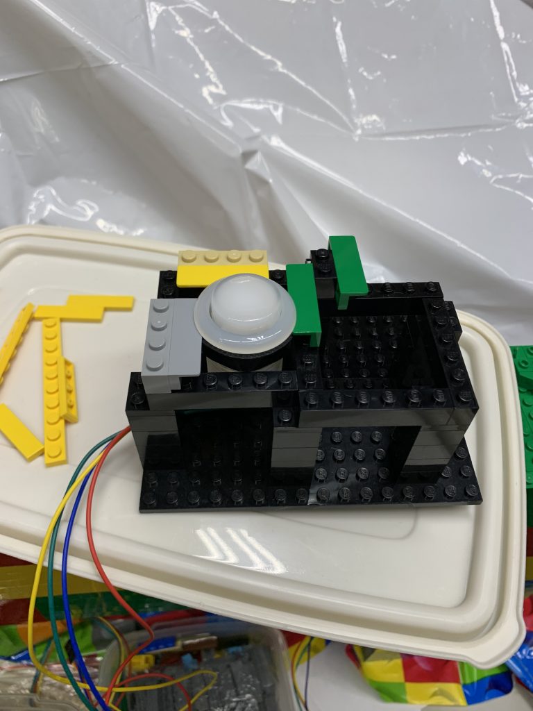 Photo of LEGO brick made into a sort of cage for buttons using L-brackets to hold the buttons in place.