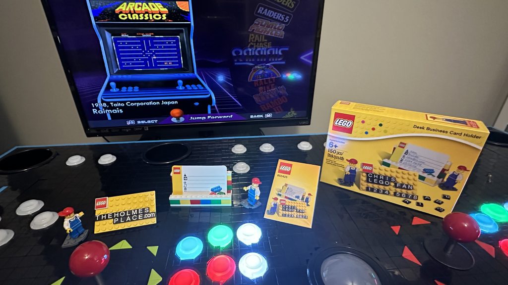 Photo showing 850425 Desk Business Card Holder set built and displayed on top of the control panel with one yellow plate displaying the lettered tiles reading, "thebrickade.com"