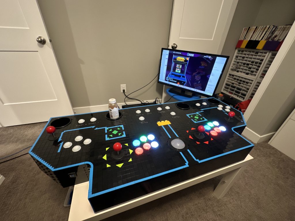 Photo of control panel, completed and buttons lit up, with tv behind it running the game system.