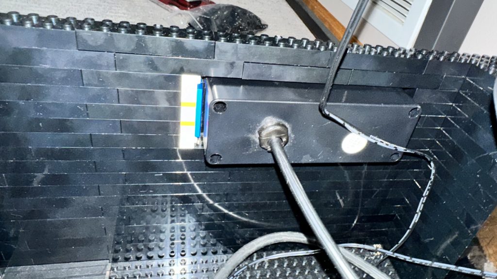 Photo showing the back of the external power supply, held in by 2x8 brick below and on top of the supply and some studs not on top pieces to the side.