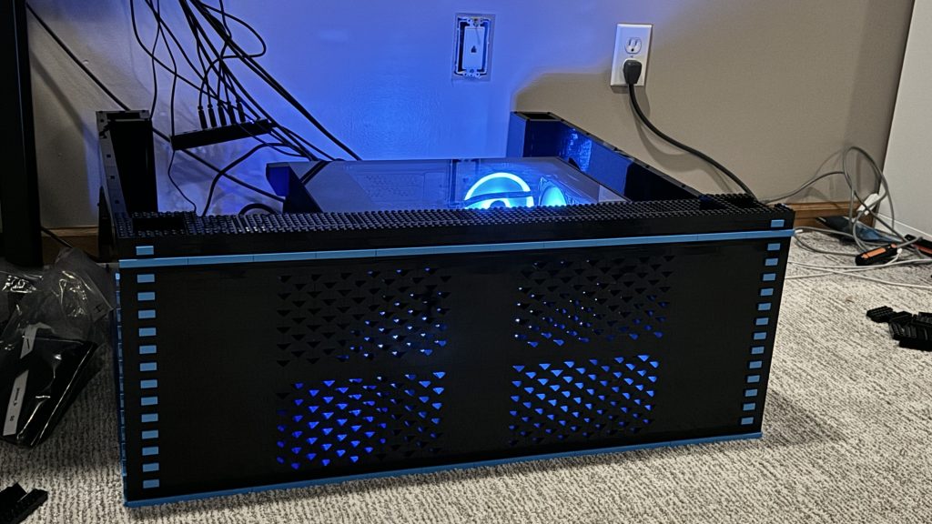 Photo of finished arcade base, showing the front, lit up behind the ventilation by the glowing LEDs of the computer.