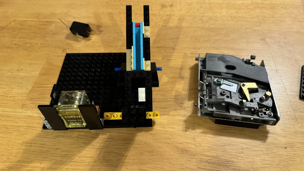 Photo taken showing another refined iteration of the LEGO® built coin chute sitting next to the mechanical coin chute. Behind them, sits a black switch
