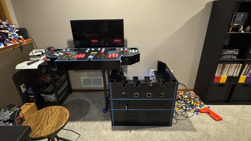Photo showing the arcade cabinet with the base on the ground, the coin bin attached above it, and the coin chutes attached above that. The control panel and LCD screen sit on a desk to the left side