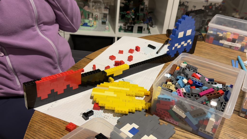 In process of building the door, showing scattered bricks on the table and a partial red ghost a broken pac-man and a blue ghost on the opposite side of the door.